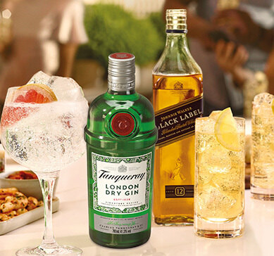 Garrafa de Johnnie Walker Black Label ao lado de garrafa de Tanqueray e de copos com drinks