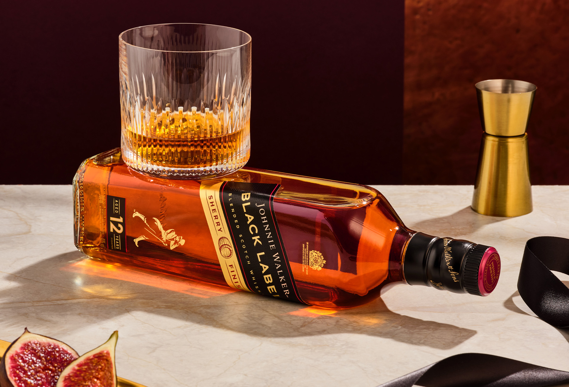 Garrafa Bebida Whisky Johnnie Walker Black Label Sherry deitado em uma mesa com um drink com gelo e whisky em cima.