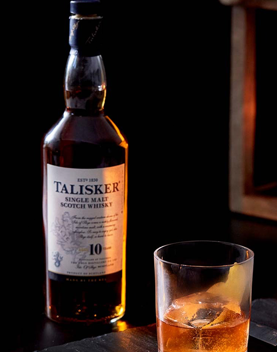 Garrafa do whisky Talisker sobre a mesa, ao lado de um copo baixo