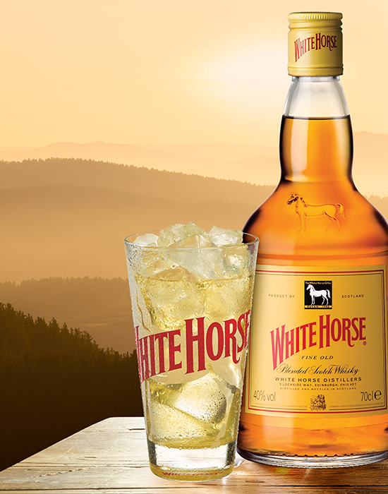 Copo alto com gelo e bebida White Horse garrafa White Horse e montanhas ao fundo