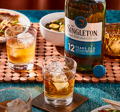Garrafa do whisky Singleton of Dufftown ao lado de dois copos com drink sobre a mesa