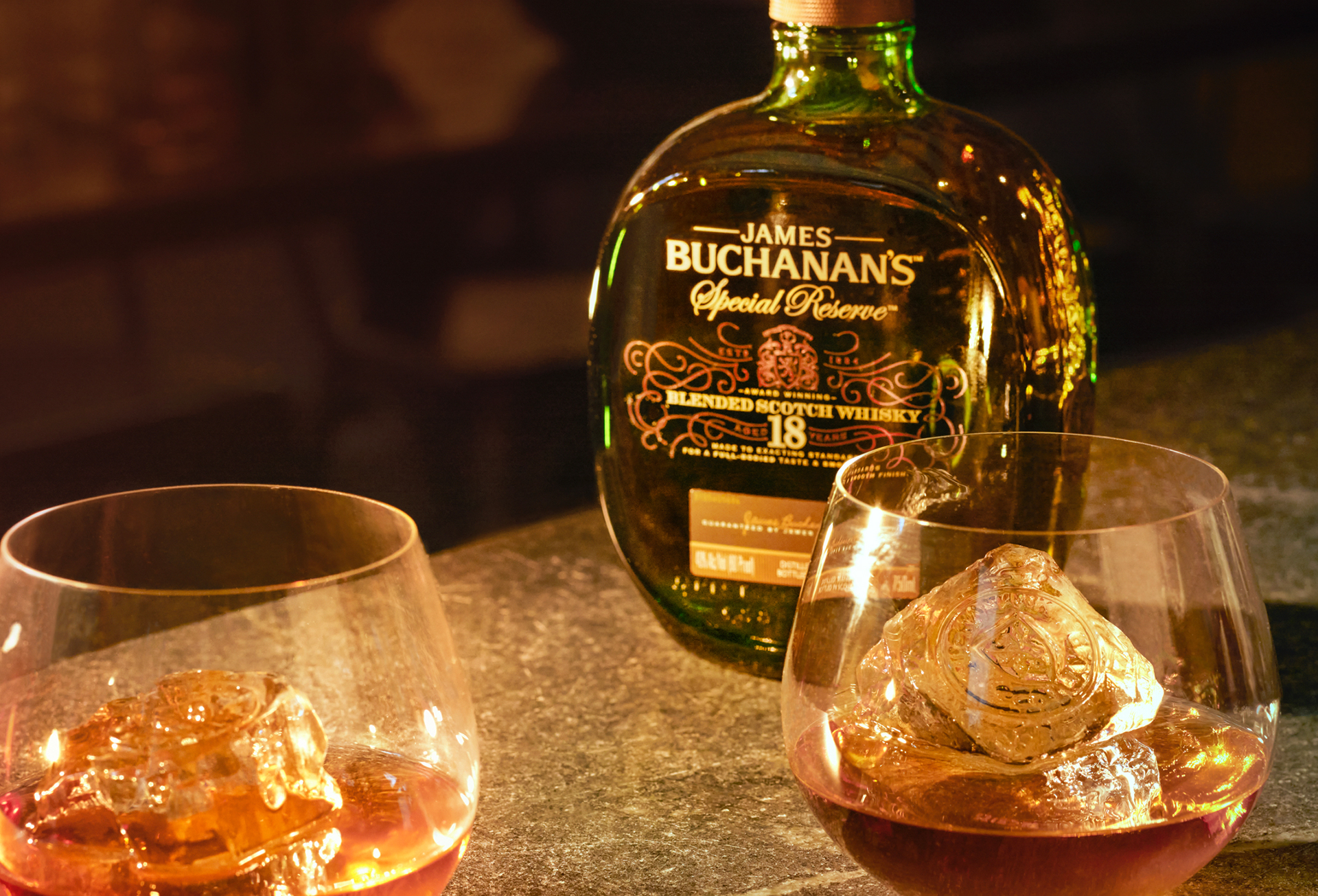 Garrafa de Buchanan's Special Reserve 18 anos com 2 drinks e copo baixo postos em mesa de mármore 