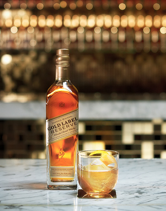 Garrafa do whisky Johnnie Walker Gold Label ao lado de um copo com drink