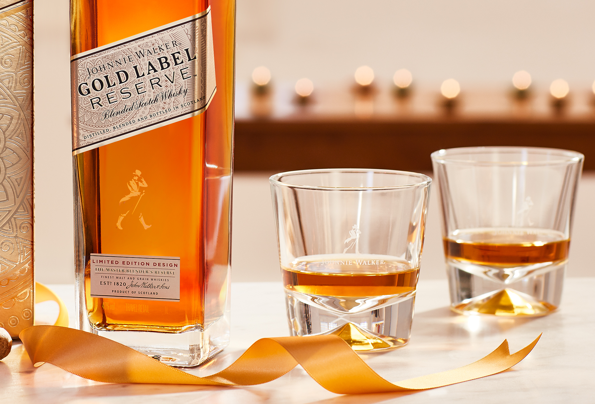 Garrafa da bebida Johnnie Walker Gold Label Reserve, com dois copos baixos de whisky e uma fita dourada.